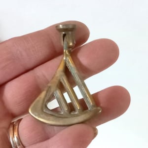 Puede incluir: Un tirador de cajón de latón vintage con un diseño triangular único. El tirador presenta una serie de barras verticales dentro del triángulo y un pequeño poste cilíndrico para la fijación. El latón tiene una pátina ligeramente envejecida.