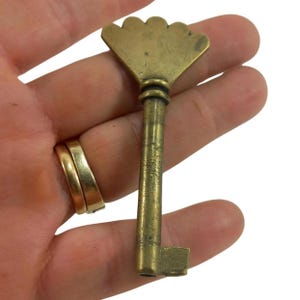 May include: Antique brass key with a decorative fan-shaped top. The key has a long, slender stem and a rectangular bit. The brass has a warm, aged patina, suggesting its vintage. A classic decorative item.