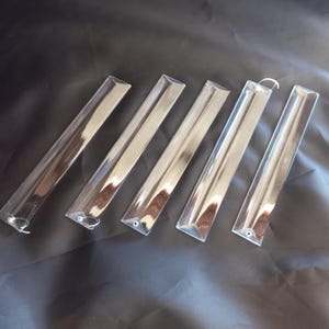 May include: Five clear, elongated glass prisms arranged in a row. Each prism features a triangular cross-section with beveled edges and a small circular hole at the top end, allowing for suspension with the attached thin silver-colored metal wire loops.