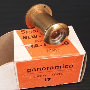 May include: A brass door viewer with a 17 mm diameter lens. The viewer is in its original packaging, which is white with orange text that reads "panoramico" and "diam. mm. 17".