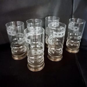 Op de afbeelding: Set van zes heldere glazen tumblers met een decoratieve witte stippenband in het midden. De basis van elk glas is metallic goudkleurig. De glazen zijn cilindrisch met een licht uitlopende bovenkant.