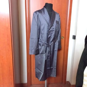 May include: A dark blue patterned robe with a shawl collar, long sleeves, and a matching belt. The robe has two front pockets and is displayed on a mannequin. The fabric has a repeating circular pattern.