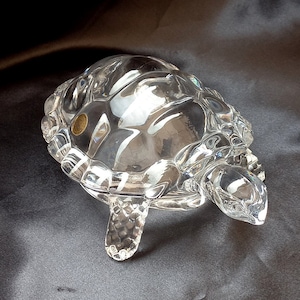 May include: A clear glass turtle figurine with a detailed shell and legs. The turtle is approximately 15 cm long and 10 cm wide.