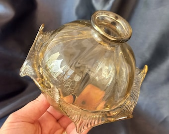 May include: A clear glass decorative bowl with a gold rim and gold accents. The bowl has a unique shape with petal-like edges. The glass has a swirl pattern. The bowl is likely used for decorative purposes.