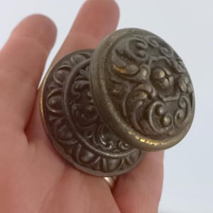Puede incluir: Un pomo de puerta vintage, adornado, de color plateado con un diseño floral detallado.