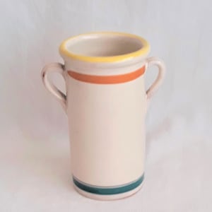 May include: A cream-colored ceramic vase with two small handles. The vase has a yellow rim, an orange stripe, and a teal stripe near the base. The vase is cylindrical in shape.