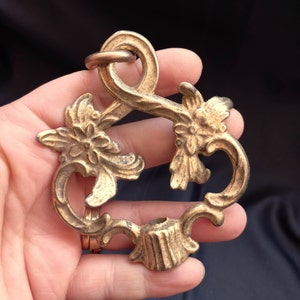 Pode incluir: Um acessório de teto decorativo de metal dourado com um design floral. O acessório tem um laço na parte superior para pendurar.
