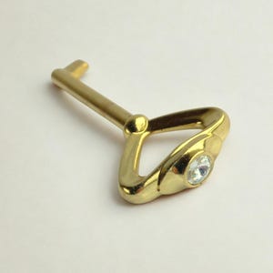 Puede incluir: Un objeto decorativo en forma de llave de color dorado con una gema redonda y transparente incrustada en el mango. La llave tiene un diseño clásico con un asa en forma de lazo y un eje recto y sencillo.