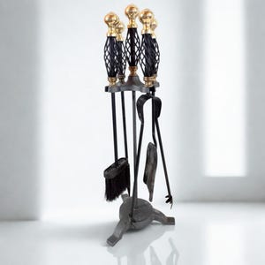 Può includere: Un set di attrezzi per camino con supporto in metallo nero e base a treppiede. Il set include una spazzola, una paletta e delle pinze, ognuna con un manico in filo nero intrecciato sormontato da un pomello sferico color oro lucido.