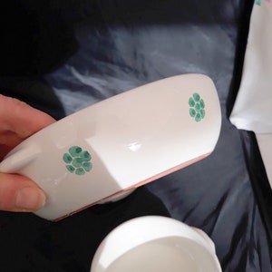May include: Two white ceramic bowls with green floral designs. The bowls are slightly different sizes and have a rustic, handmade look.