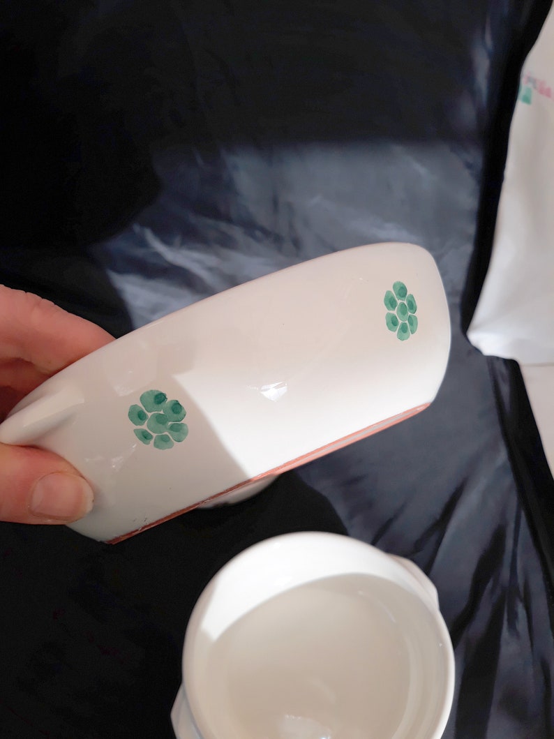 May include: Two white ceramic bowls with green floral designs. The bowls are slightly different sizes and have a rustic, handmade look.