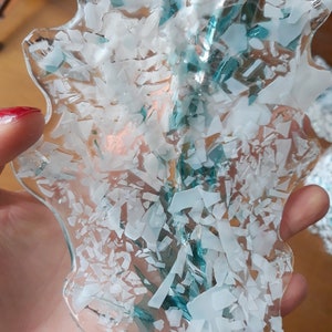 K&ouml;nnte beinhalten: Ein klares, unregelm&auml;&szlig;ig geformtes Glasobjekt mit einem Muster aus wei&szlig;en und hellblauen Fragmenten. Das Objekt wird in einer Hand gehalten, der Hintergrund ist unscharf.