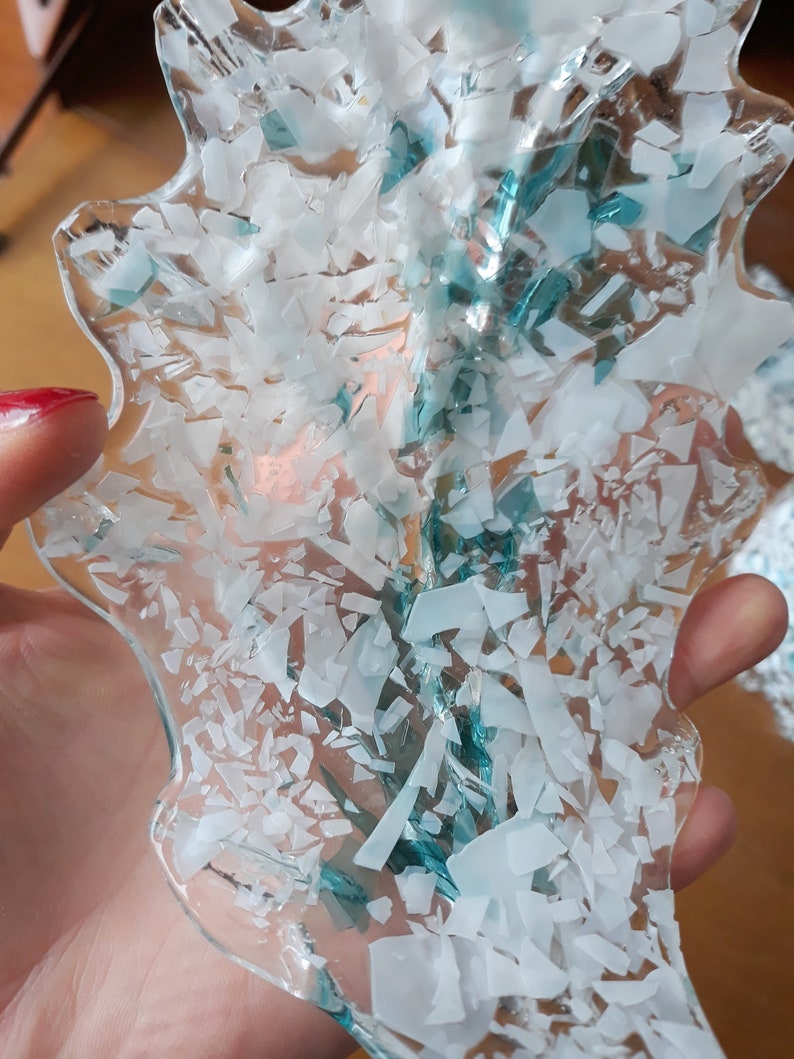 K&ouml;nnte beinhalten: Ein klares, unregelm&auml;&szlig;ig geformtes Glasobjekt mit einem Muster aus wei&szlig;en und hellblauen Fragmenten. Das Objekt wird in einer Hand gehalten, der Hintergrund ist unscharf.