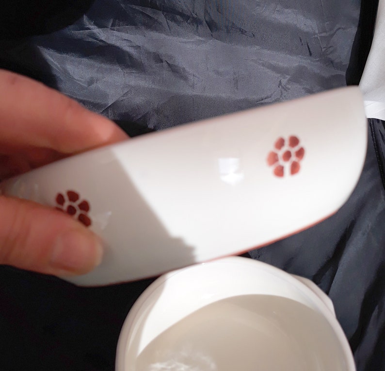 May include: White ceramic bowl with a red floral design. The bowl is slightly curved and has a lip around the edge.