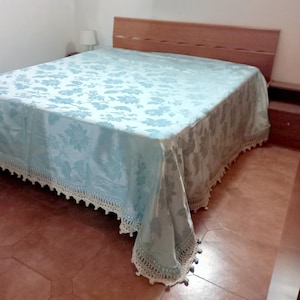 Può includere: Un letto con un copriletto a fantasia floreale azzurro e una testiera in legno. Il copriletto ha un bordo in pizzo bianco. La stanza ha una lampada su un comodino.