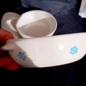 May include: White ceramic bowl with a blue floral design. The bowl has a rounded shape and a slightly raised rim.