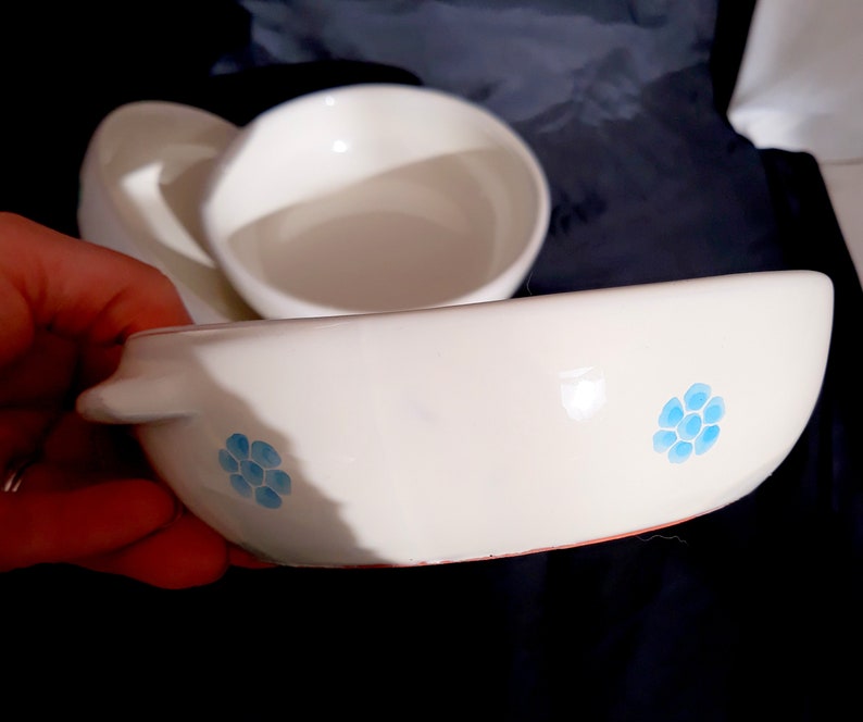 May include: White ceramic bowl with a blue floral design. The bowl has a rounded shape and a slightly raised rim.