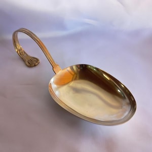 Peut inclure: Une louche dorée avec une poignée incurvée et un motif floral décoratif à l'extrémité. La louche a un grand bol de forme ovale. La poignée est incurvée et présente un motif strié.