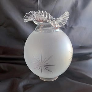 May include: A spherical glass lamp shade featuring a frosted finish with etched starburst patterns. The top of the shade has a clear, ruffled, and crimped edge design. The body is round and opaque, contrasting with the transparent, wavy rim.