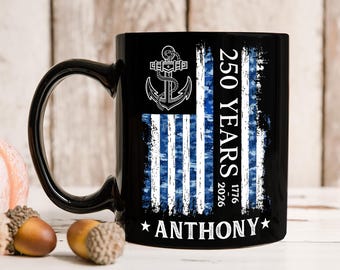Op de afbeelding: Een zwarte keramische mok met een afbeelding van een blauw-witte verweerde vlag met een ankersymbool. De tekst luidt 250 YEARS, 1776-2026, en de naam ANTHONY staat onderaan tussen twee witte sterren gedrukt in een vetgedrukt hoofdlettertype.
