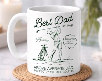 Op de afbeelding: Een witte keramische mok met donkergroene tekst en een afbeelding van een golfer. De tekst luidt Best Dad BY PAR, Anthony, RANKED NO.1 BY FAMILY en ABOVE AVERAGE DAD. PERFECTLY AVERAGE GOLFER. Het ontwerp toont een golfer die een club zwaait.