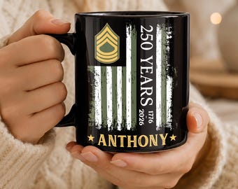 Op de afbeelding: Een zwarte keramische mok met een verweerd Amerikaans vlagontwerp in olijfgroen en wit. De afbeelding bevat een militair ranginsigne, de tekst 250 YEARS, de jaartallen 1776 en 2026, en de naam ANTHONY in gouden letters met sterren aan weerszijden.