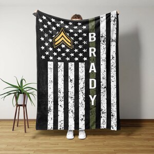 May include: A black and white American flag with a green stripe down the right side. The stripe has the name "BRADY" written in white letters. The flag has a gold sergeant chevron in the top left corner.