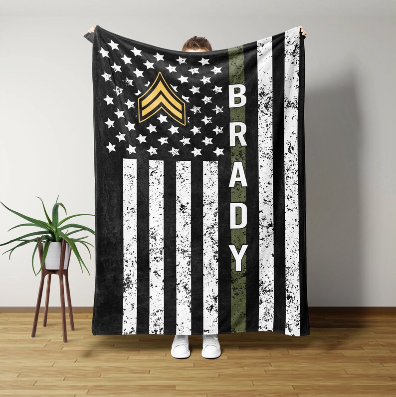 May include: A black and white American flag with a green stripe down the right side. The stripe has the name "BRADY" written in white letters. The flag has a gold sergeant chevron in the top left corner.