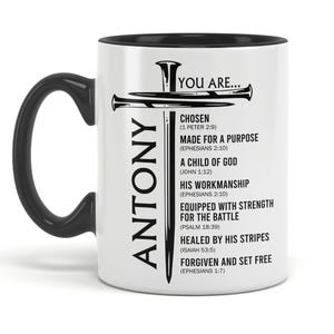 May include: White ceramic mug with a black handle and rim. The mug features the name "ANTONY" in black vertical text and a cross design. Text on the mug includes "YOU ARE..." and various inspirational phrases.
