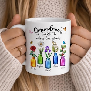 May include: White ceramic mug featuring the text "Grandma's Garden where love grows." The mug has colorful illustrations of flowers in vases, with names below each. Butterflies are also included in the design.