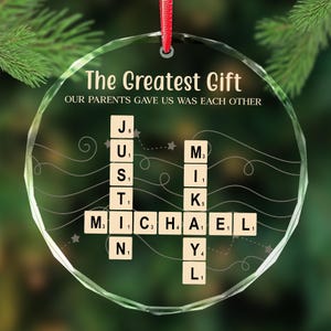 May include: A clear, round Christmas ornament with the text "The Greatest Gift" and "OUR PARENTS GAVE US WAS EACH OTHER". The names "JUSTIN MICHAEL" are spelled out with letter tiles. A red ribbon is attached for hanging.