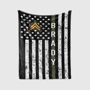 May include: Black and white American flag fleece blanket with a green stripe down the right side. The stripe has the name "BRADY" printed on it. A gold military rank insignia is in the upper left corner.