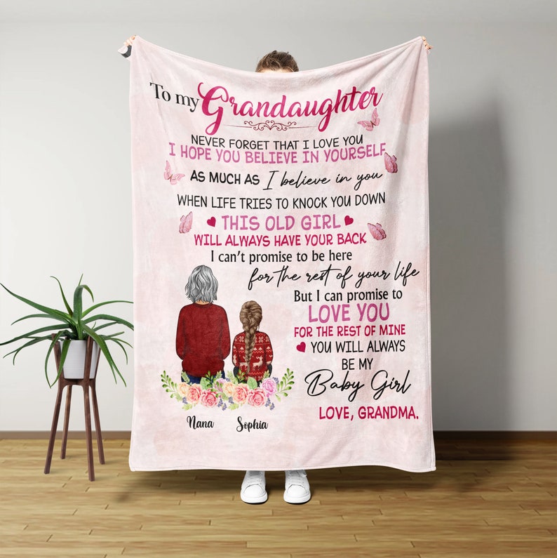 May include: Pink and white fleece blanket with a message to a granddaughter. The message reads "To my Grandaughter Never forget that I love you I hope you believe in yourself as much as I believe in you When life tries to knock you down This old girl will always have your back I can't promise to be here for the rest of your life But I can promise to love you for the rest of mine You will always be my Baby Girl Love, Grandma." The blanket features a cartoon illustration of two women, one with gray hair and the other with brown hair, sitting on a bench with flowers.