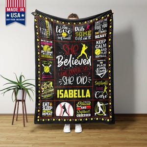May include: Black softball blanket with various softball-themed graphics and text. The blanket features phrases like "She Believed, She Did," and "Softball Hair Don't Care." The name "Isabella" is prominently displayed.