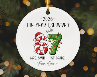 Op de afbeelding: Een rond wit keramieken ornament met een gouden koord. Het bevat de tekst 2026 THE YEAR I SURVIVED BARELY, het getal 67 als zuurstok met kerstmuts en kerstverlichting, en de tekst MRS. SMITH - 1ST GRADE From Olivia.