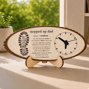 May include: A wooden clock with a natural edge, featuring a clock face and text that reads "stepped up dad". The clock includes a stand and a footprint graphic. The clock's hands show the time.