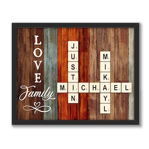 May include: A rustic wooden sign with the word "LOVE" spelled vertically in white letters. Below the word "LOVE" is the word "Family" in cursive script with a heart symbol. The sign also features a scrabble tile crossword puzzle with the names "JUSTIN" and "MICHAEL" spelled out.
