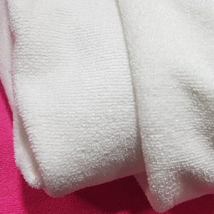 May include: Two white microfiber cloths folded on a pink surface. The cloths are soft and absorbent, ideal for cleaning and drying.