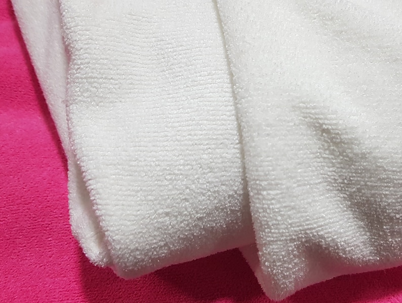 May include: Two white microfiber cloths folded on a pink surface. The cloths are soft and absorbent, ideal for cleaning and drying.