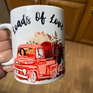 May include: White ceramic mug with a red pickup truck carrying flowers and a couple inside. The mug has the words "Loads of Love" written on it.