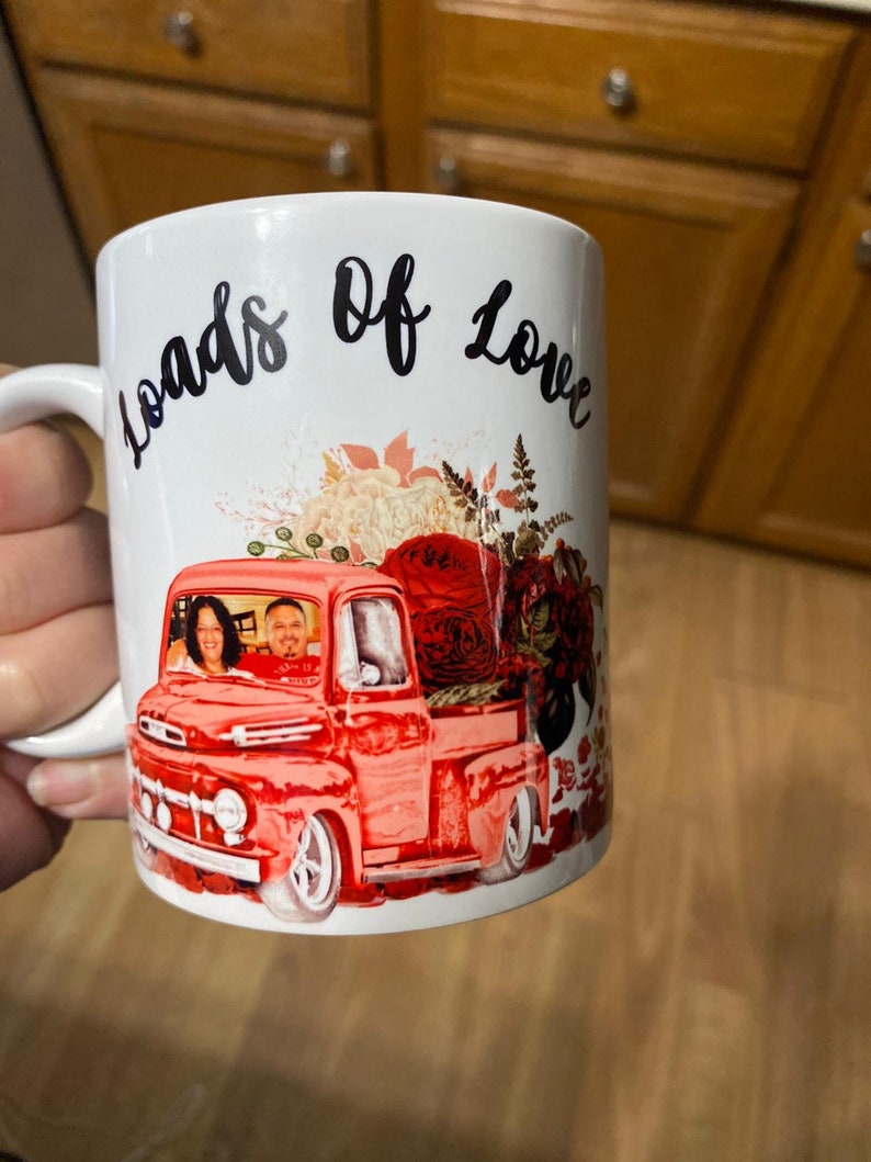 May include: White ceramic mug with a red pickup truck carrying flowers and a couple inside. The mug has the words "Loads of Love" written on it.