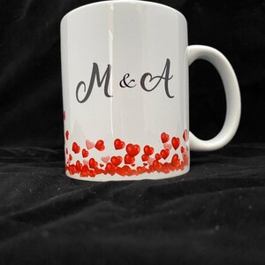 May include: White ceramic mug with a black inscription "M & A" and a border of red hearts.