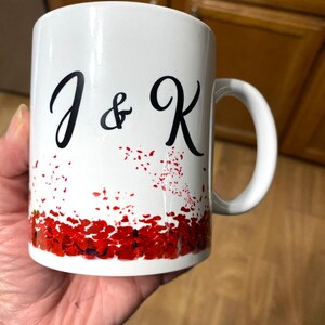 May include: White ceramic mug with a black design of "J & K" and a red and white confetti pattern around the bottom.