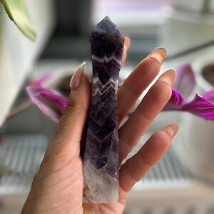 Könnte beinhalten: Eine violette Amethyst-Kristallspitze mit weißen und violetten Bändern. Der Kristall ist oben spitz und hat einen flachen Boden.