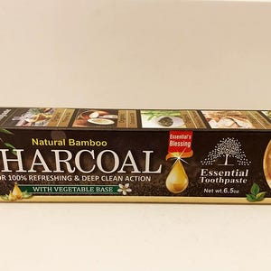May include: A rectangular box of Natural Bamboo Charcoal toothpaste. The box is dark brown with white text and images of bamboo, a drop, and a tree. The text reads "Essential Toothpaste" and "New 5 in 1 Organic".