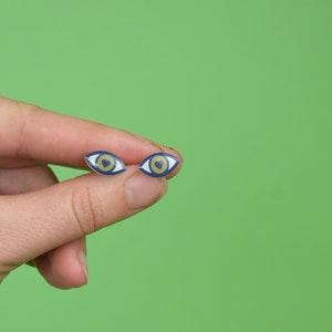 Pode incluir: Um par de brincos em forma de olho azul e dourado com um coração no centro de cada olho.