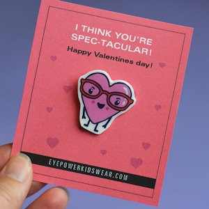 May include: Pink heart-shaped character wearing red glasses with the text "I think you're SPEC-TACULAR! Happy Valentines day!" and the website "EYEPOWERKIDSWEAR.COM" on a pink card.