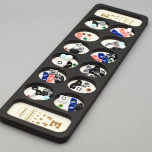 May include: Black eye chart with 12 oval-shaped compartments filled with colorful plastic shapes. The chart is labeled "Eye Chart" and has the letter "E" printed on the bottom.