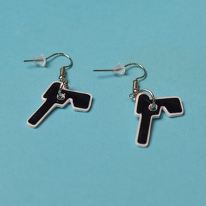 Pode incluir: Um par de brincos em forma de chave preto e branco com ganchos prateados.