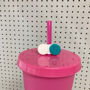 Puede incluir: Un vaso reutilizable rosa con tapa y una pajita. La tapa tiene dos pequeños estuches redondos para lentes de contacto, uno blanco y otro turquesa.